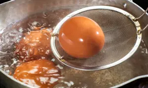 Jajka na miękko gotują się w garnku. Jedno jajko jest wyjmowane sitkiem.