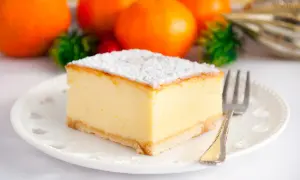 Puszysty sernik z wiaderka, posypany cukrem pudrem, na talerzyku z widelcem. W tle pomarańcze i ozdoby.
