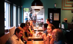 Ludzie siedzą przy stołach w przytulnym bistro, rozmawiają i piją.