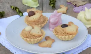 Wielkanocne babeczki z mascarpone, ozdobione ciasteczkami w kształcie króliczków i czekoladowymi jajeczkami, na talerzu wśród ceramicznych zajączków.