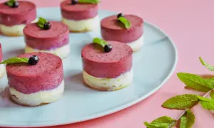 Urocze mini serniczki z jagodami i miętą na jasnoniebieskim talerzu, gotowe do degustacji.