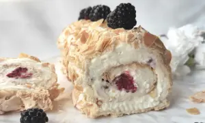Rolada bezowa z malinami i jeżynami, posypana płatkami migdałów, wygląda apetycznie.