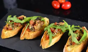 Hiszpańskie tapas kanapeczki z pomidorami, rukolą i ziołami, ułożone na czarnym kamieniu.