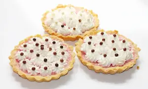 Trzy apetyczne tartaletki z owocami i galaretką, ozdobione bitą śmietaną i czekoladowymi kuleczkami.