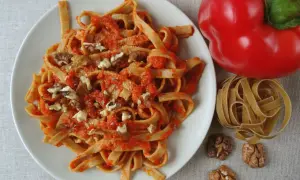 Pyszne spaghetti z papryką i orzechami włoskimi, obok czerwona papryka i surowy makaron.