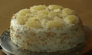 Pyszny tort z ananasem, udekorowany kawałkami owoców i posypką orzechową, prezentuje się apetycznie na metalowej podstawie.