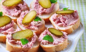 Kromki chleba z pyszną pastą z szynki, ozdobione plasterkami ogórka kiszonego i natką pietruszki. Idealna przekąska!