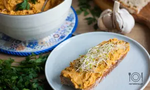 Pyszna pasta z kurczaka na kromce chleba, posypana kiełkami. Obok miska z pastą, czosnek i natka pietruszki.