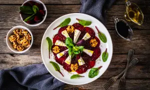 Eleganckie carpaccio z buraka z serem feta, orzechami włoskimi i świeżymi ziołami, podane na białym talerzu.