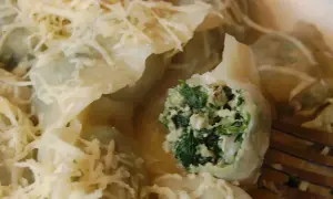 Pyszne pierogi z kurczakiem i szpinakiem, polane sosem i posypane startym serem. Jeden pieróg jest przekrojony, ukazując bogate nadzienie.
