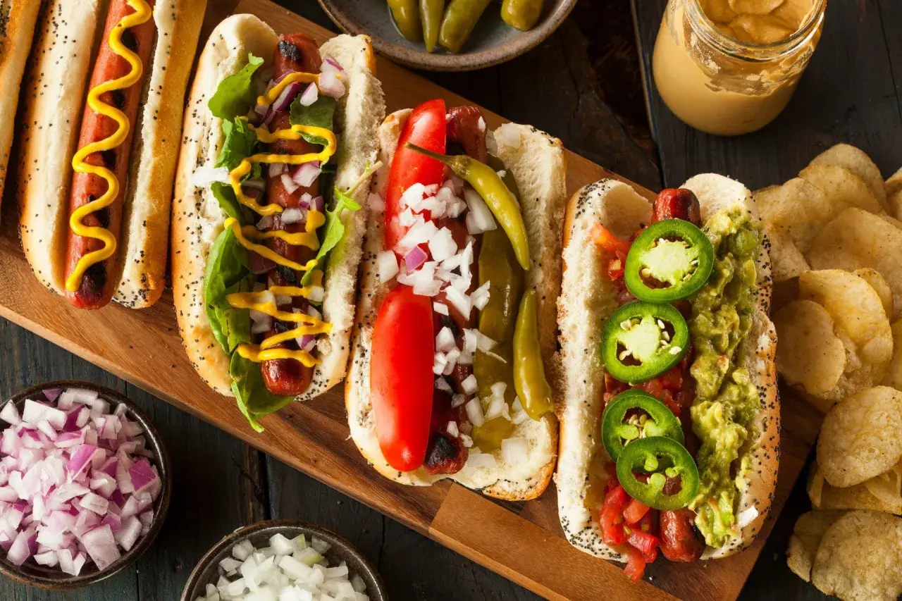 Cztery pyszne hot dogi z różnymi dodatkami: musztarda, cebula, pomidor, papryczki i guacamole.