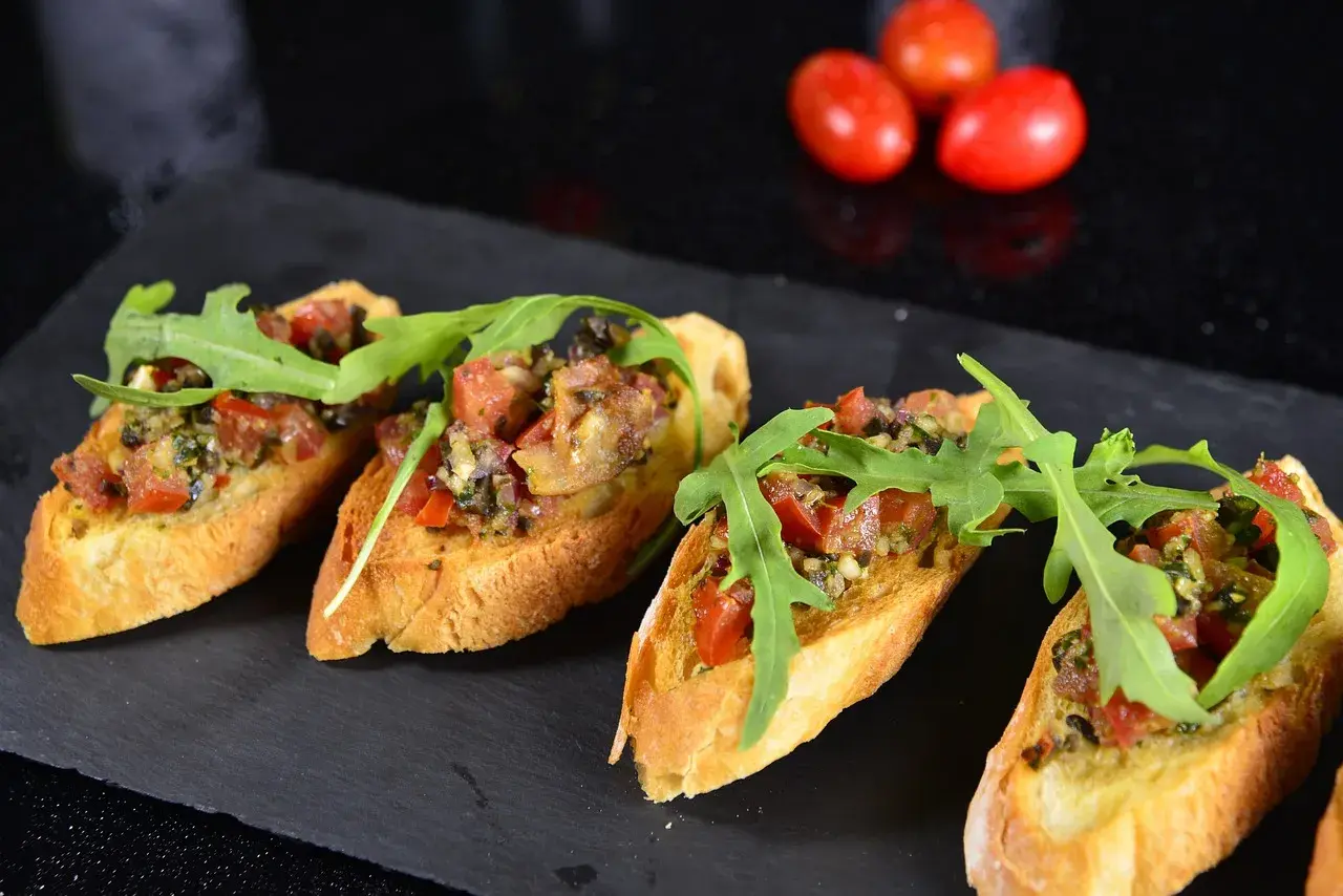 Hiszpańskie tapas kanapeczki z pomidorami, rukolą i ziołami, ułożone na czarnym kamieniu.