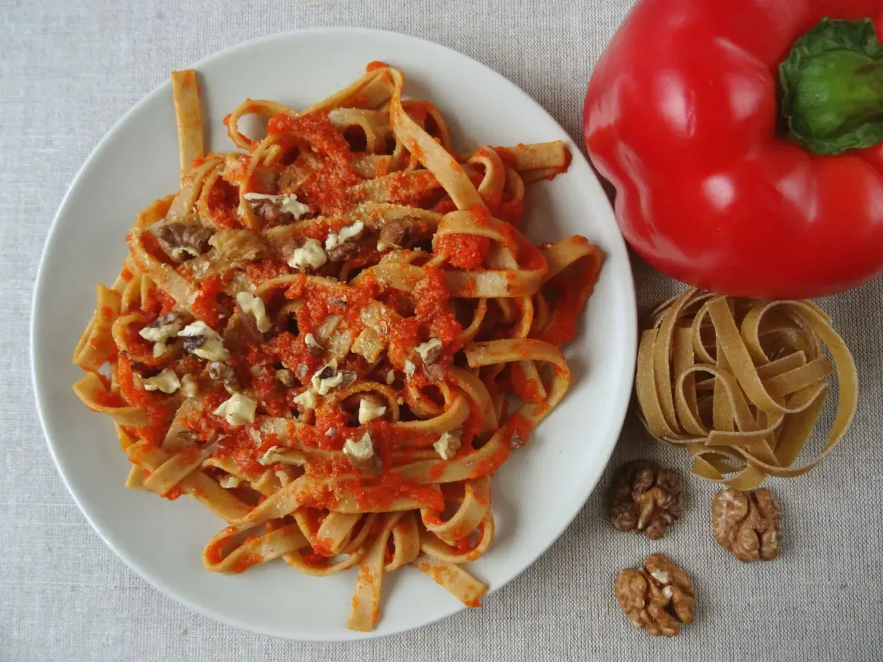 Pyszne spaghetti z papryką i orzechami włoskimi, obok czerwona papryka i surowy makaron.