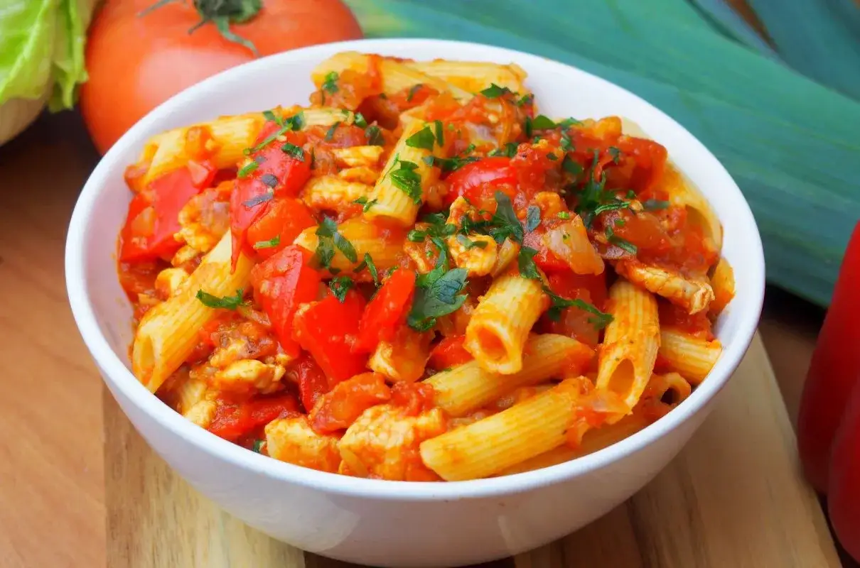 Penne z kurczakiem i papryką w sosie pomidorowym, posypane natką pietruszki. Pyszne danie na obiad.