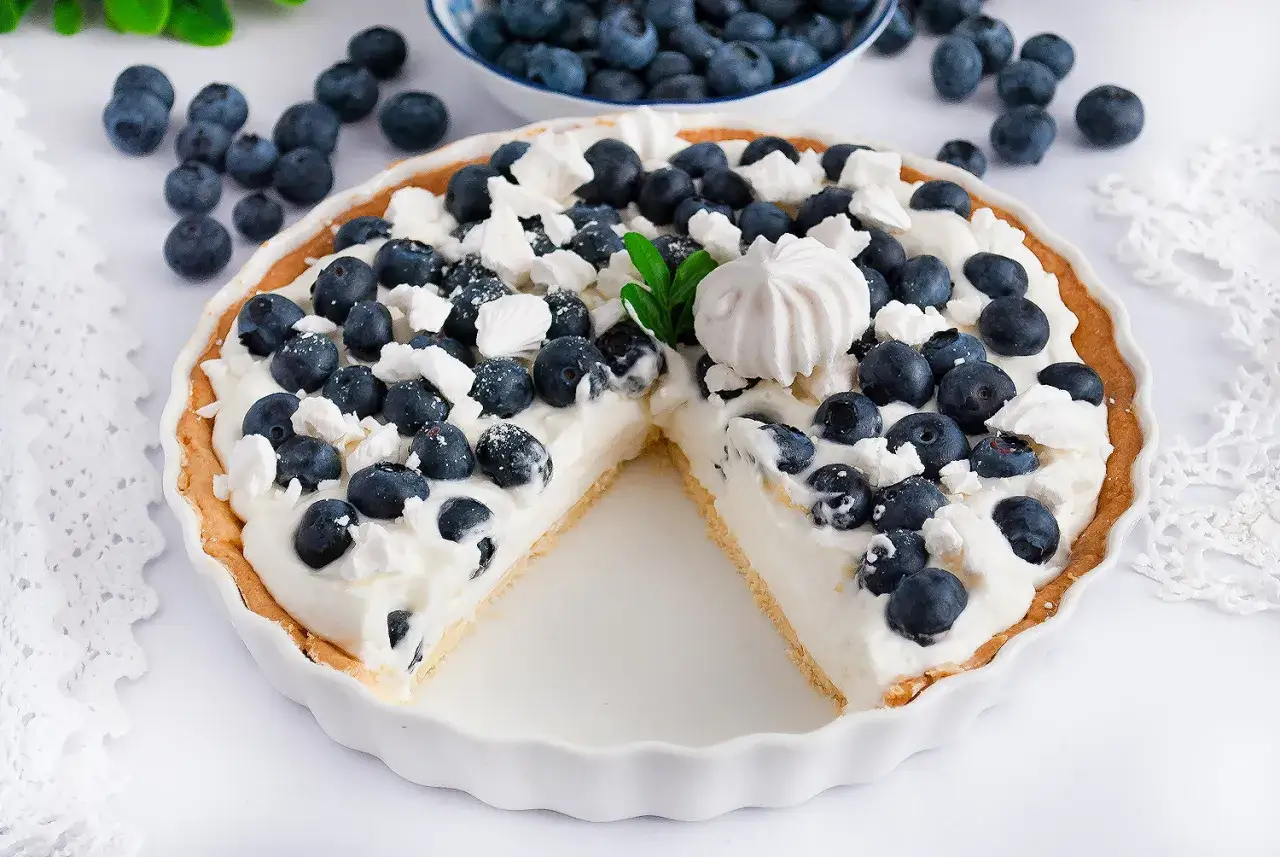 Pyszna tarta z borówkami, udekorowana bitą śmietaną i bezą. Idealna na letnie popołudnie.