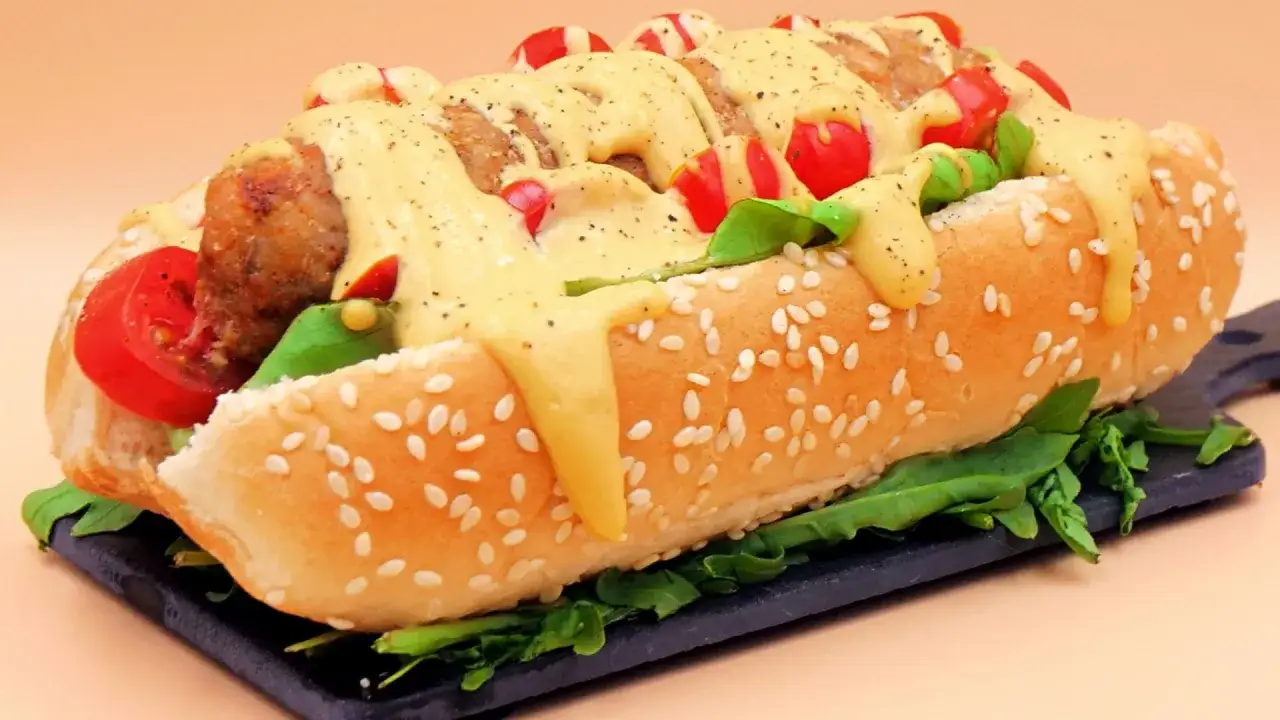 Pyszny hot dog z kiełbaską, pomidorkami, rukolą i obficie polany sosem serowym.