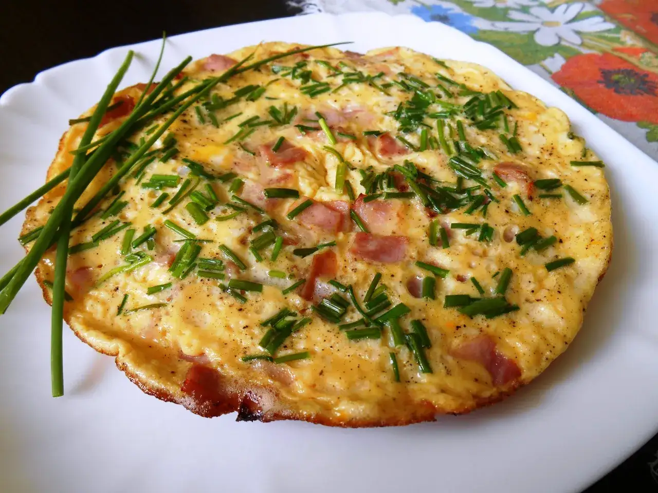 Pyszny omlet ze szczypiorkiem i kawałkami wędliny, podany na białym talerzu.