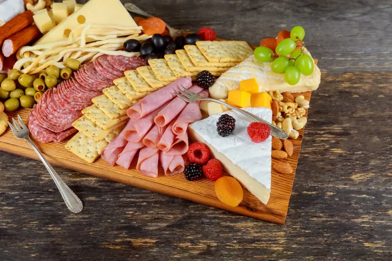 Apetyczna deska serów i wędlin: salami, szynka, sery, oliwki, winogrona, orzechy i owoce. Idealna na spotkanie.