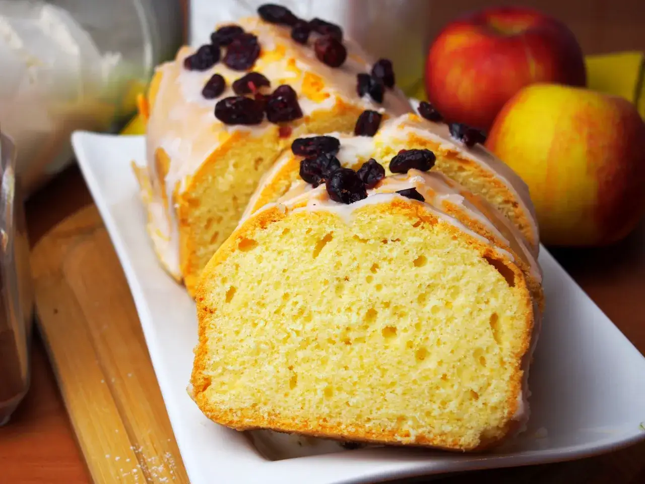 Pyszna babka na oleju z lukrem i żurawiną, pokrojona w plastry, obok jabłek.