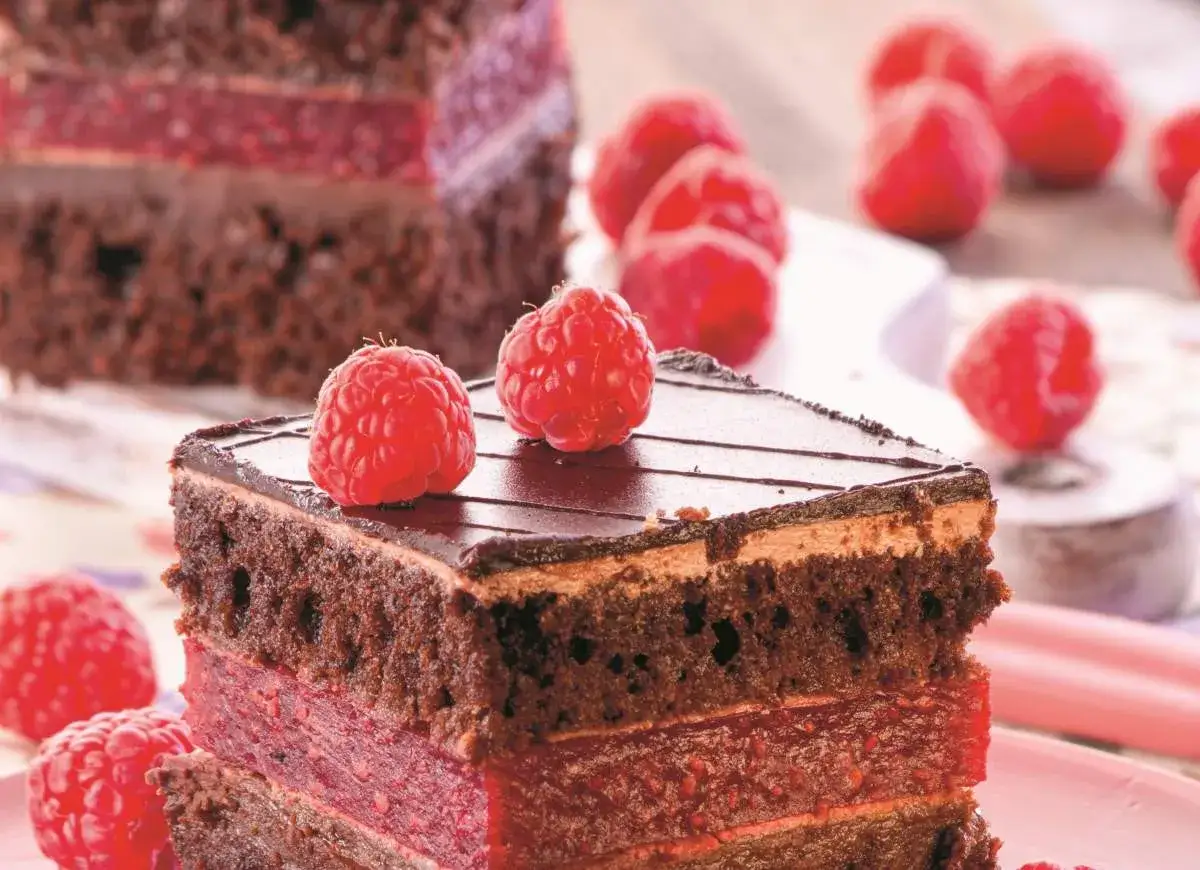 Pyszny brownie z malinami, przełożony warstwami owocowej masy, ozdobiony świeżymi malinami i polewą czekoladową.