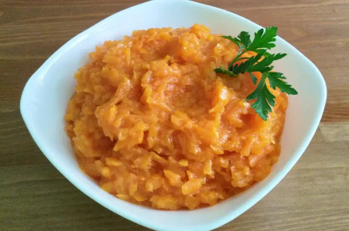 Pyszna, starte marchewka do obiadu, udekorowana gałązką natki pietruszki.