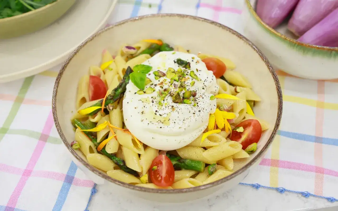 Penne z burratą, szparagami i pomidorkami koktajlowymi, posypane pistacjami. Pyszne danie, które zachwyci każdego miłośnika makaronu ze szparagami.