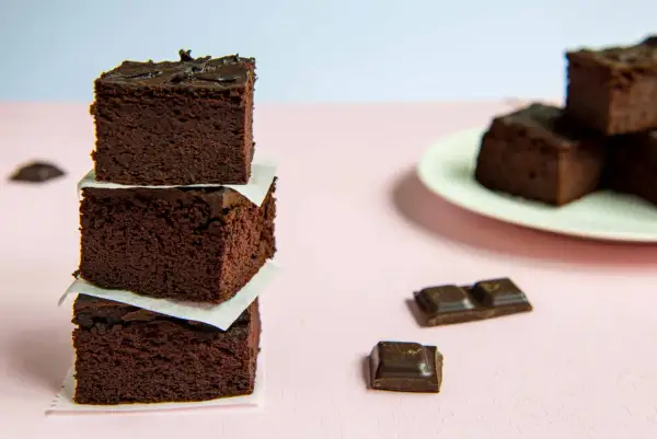 Ciemne, wilgotne brownie z fasoli, ułożone w stosik, obok kawałków czekolady.