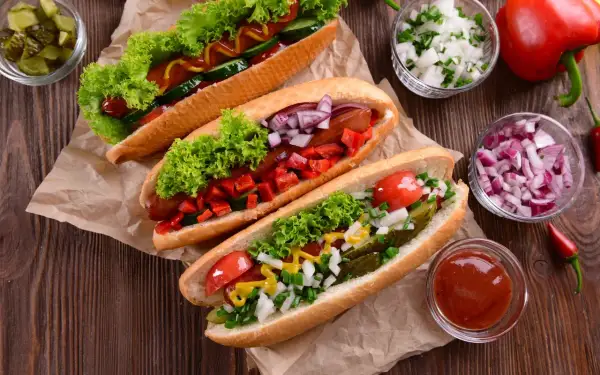 Trzy apetyczne hot dogi z sałatą, pomidorami, ogórkiem, cebulą i papryką. Idealne na letnie grillowanie!